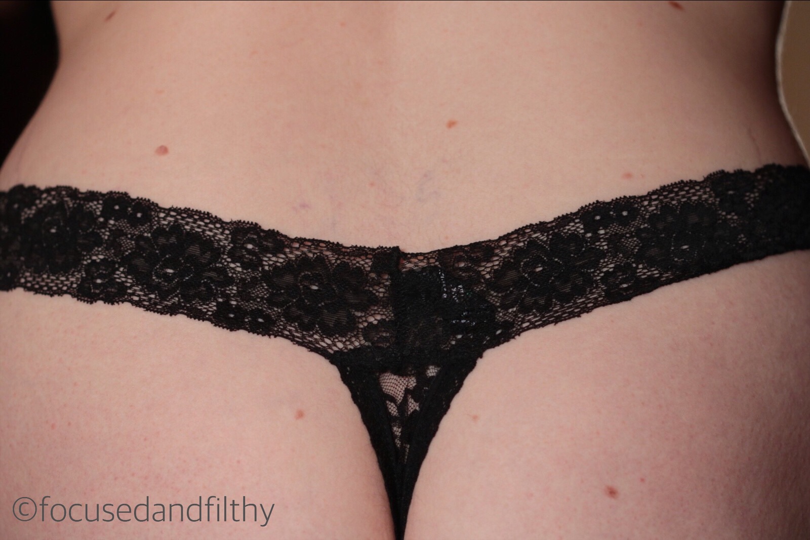 Close up colour image of a small section of black lacy knickers and the top of a rounded curvy arse