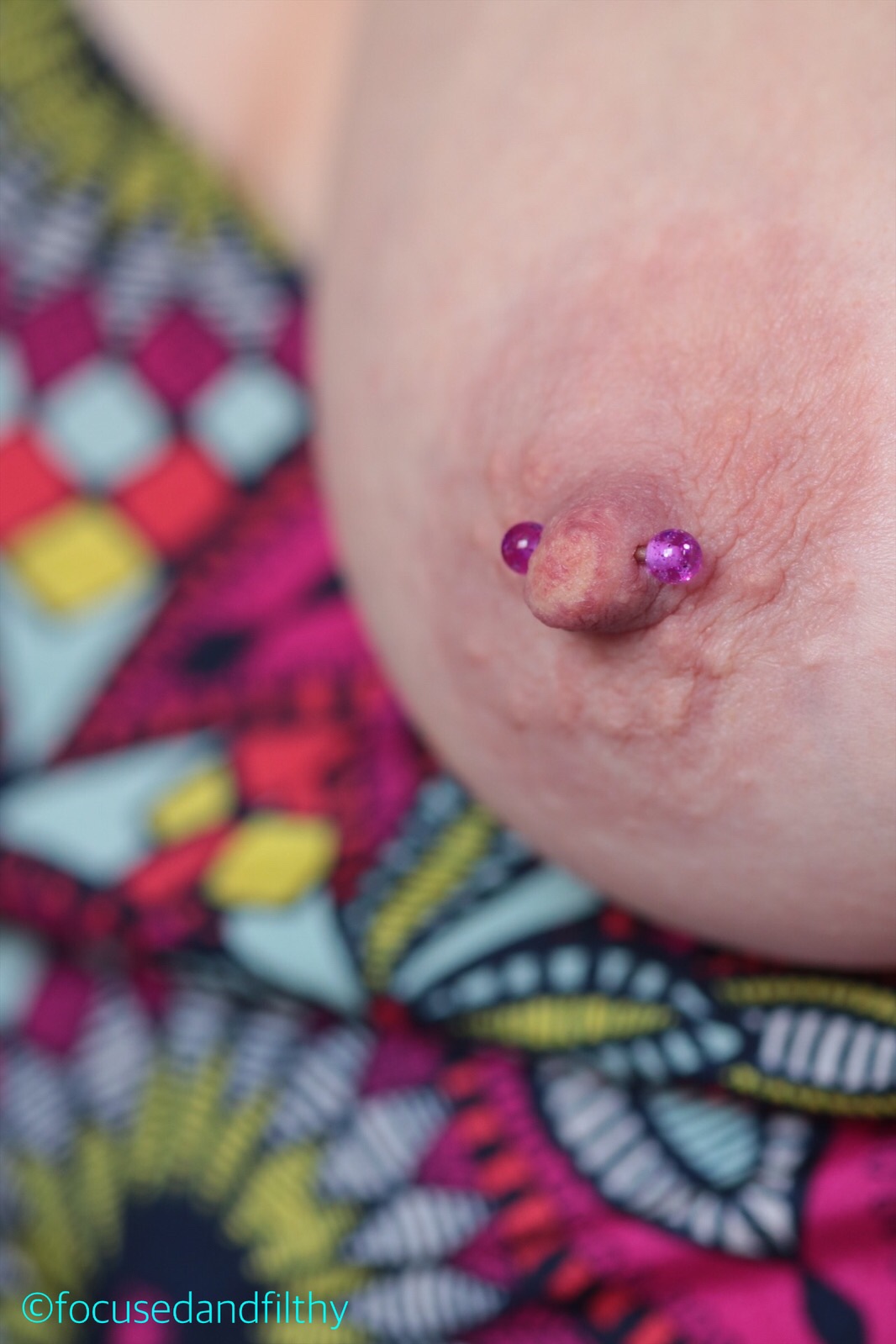 Close up colour photograph of a left female nipple and breast with a pink balled nipple bar 
