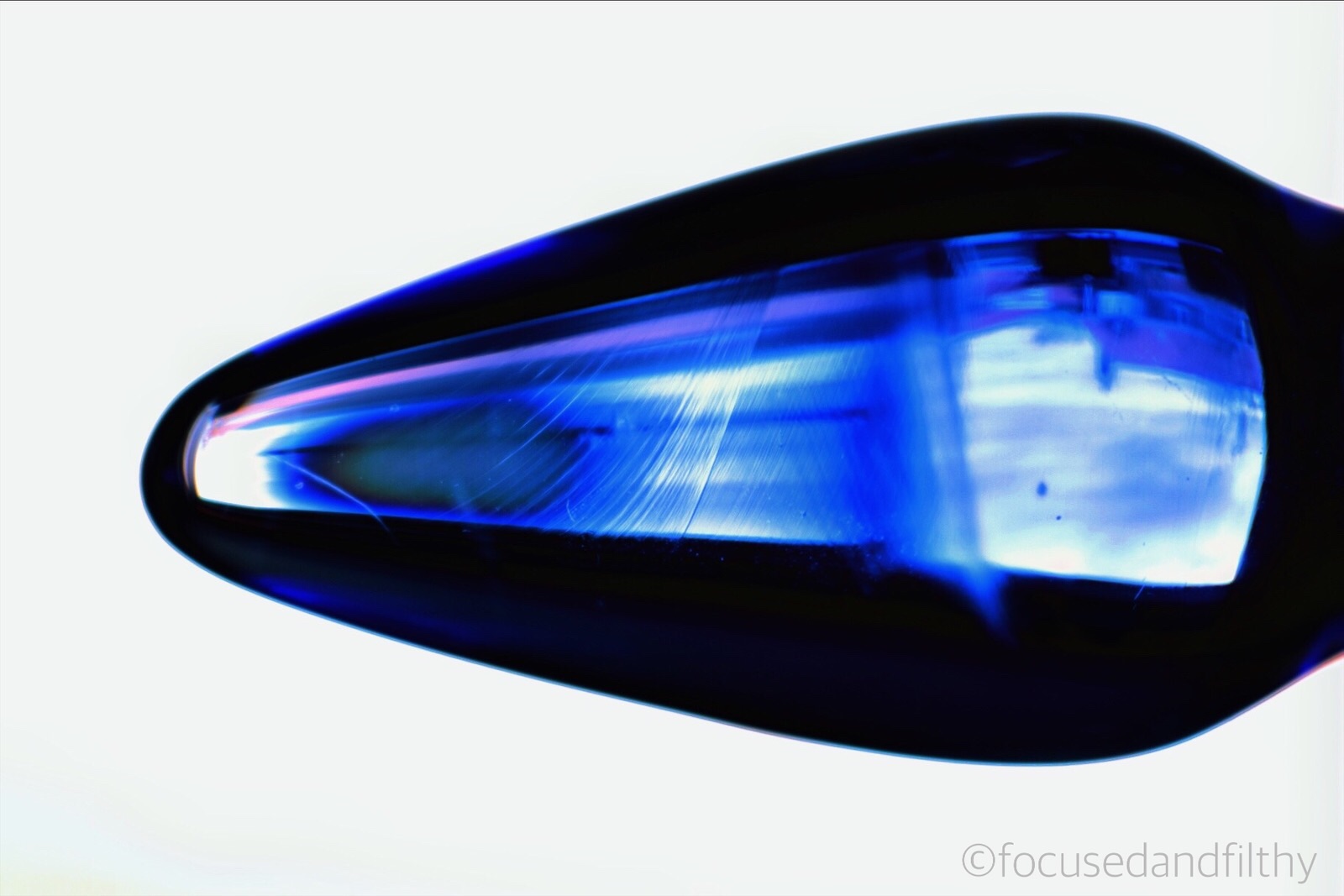 Close up colour photograph of just the tip of a blue glass butt plug which is slightly see through and like a torpedo tip