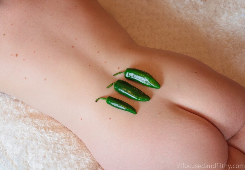 Colour photograph of my naked back and arse with three small green chillis  in a row  