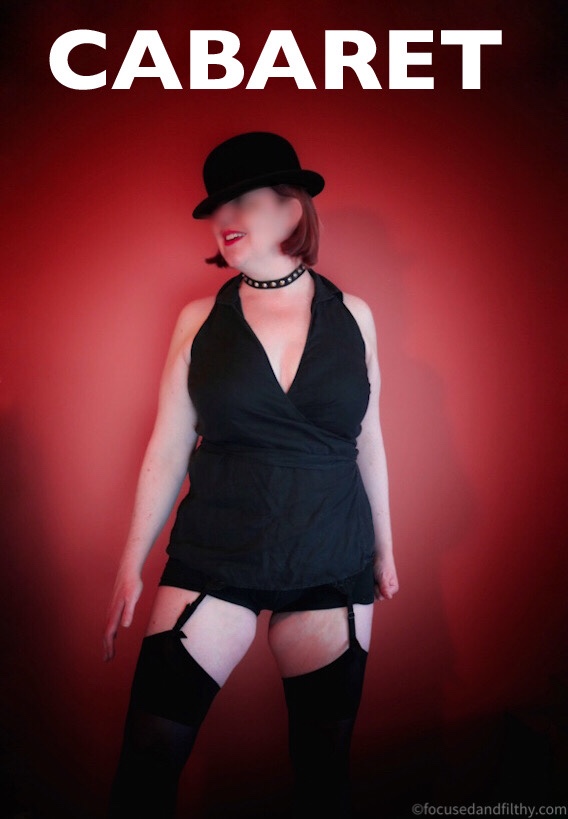 Colour photograph of a woman  in a spot light against a red background in black halter neck top, stockings and suspenders and a bowler hat  