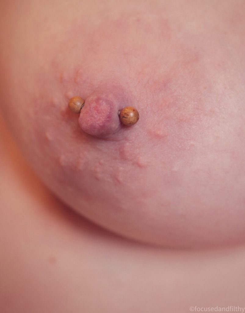 Close up colour photograph of my left nipple with a nipple bar in with small teak wooden ball ends on it  