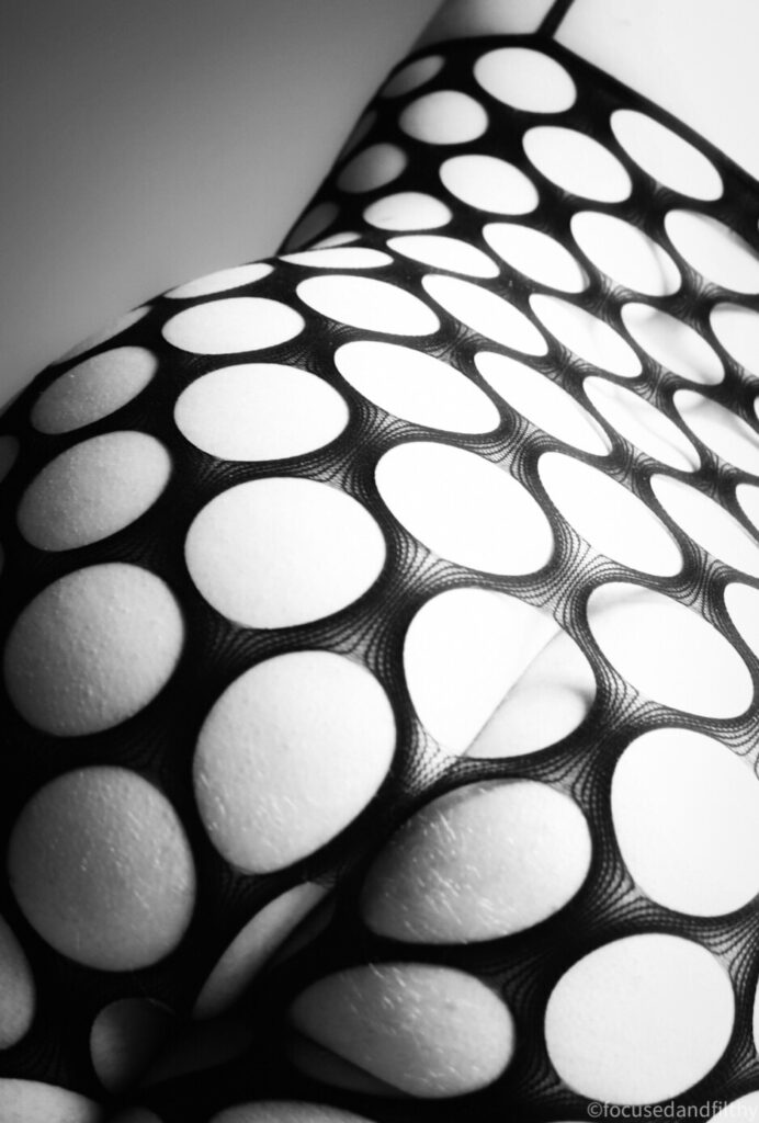 A black and white close up photograph of a bum and back wearing a larger holed bodystocking 