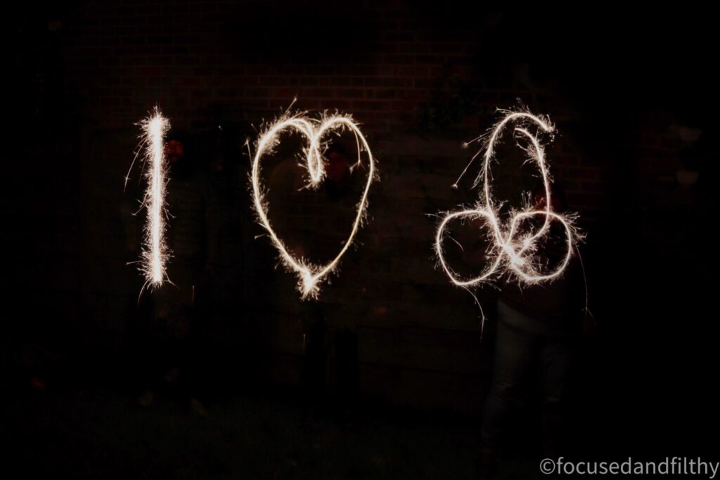 A photograph of three people holding sparklers making a sign. The image is very dark and only the sparklers show up. It says I love (with a heart) Cock. The cock is drawn with penis and balls. 