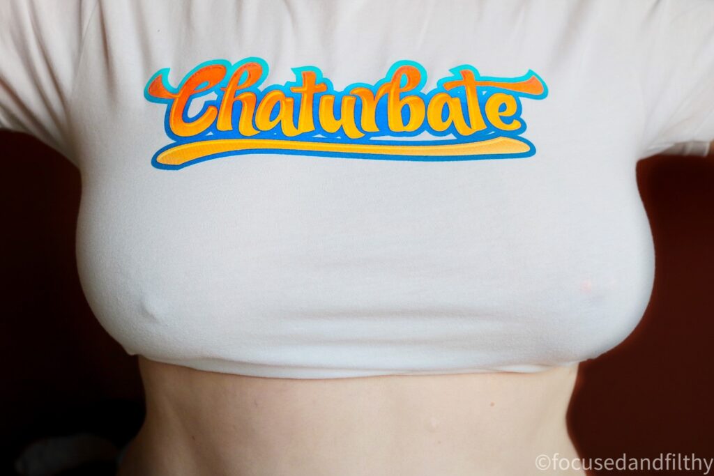 A close up colour photograph of my chest in a white TShirt with the word Chaturbate across it in large orange letters. The T-shirt is pulled tight so my breasts are obviously large with prominent nipples. 