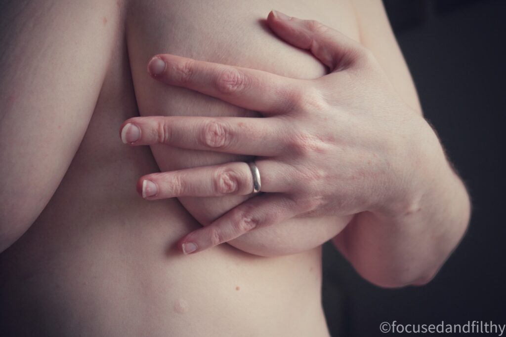 A colour close up photograph of my naked left breast with my hand covering the nipple 