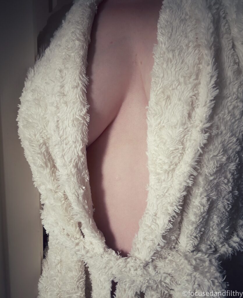 A colour close up photograph of my torso wrapped in my fluffy white dressing gown , it’s just open enough to see the swell of my naked breasts. 
