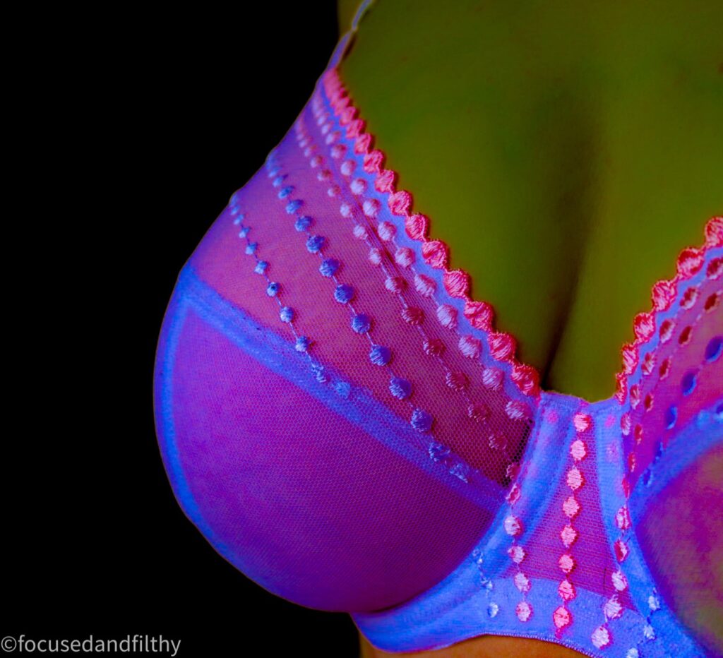A close up photograph of a bra which has been edited to look bright illuminous  pink against my skin which looks slightly dark green 