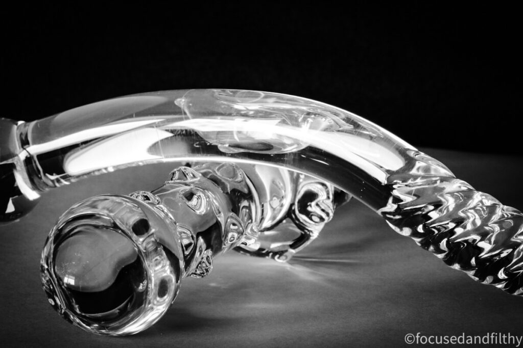 A close up black and white photograph of two glass toys next to each other.  One is covered in small raised dimples and the other is thin and curved with a ridged textured end. 