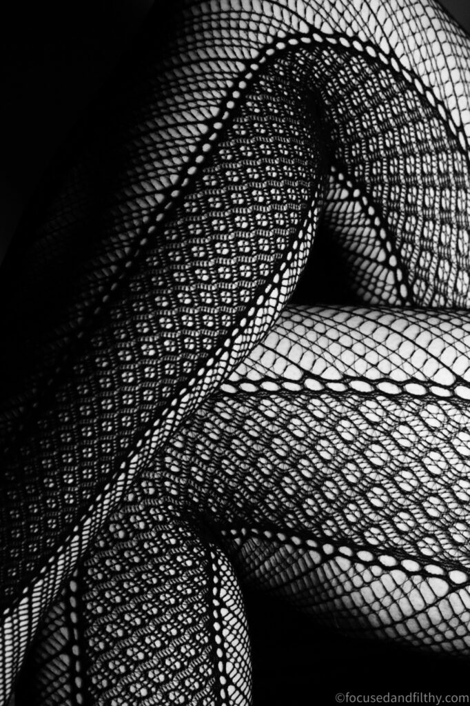 A close up black and white photograph of my crossed legs wearing fishnet tights with interesting side patterns that add to the look. 