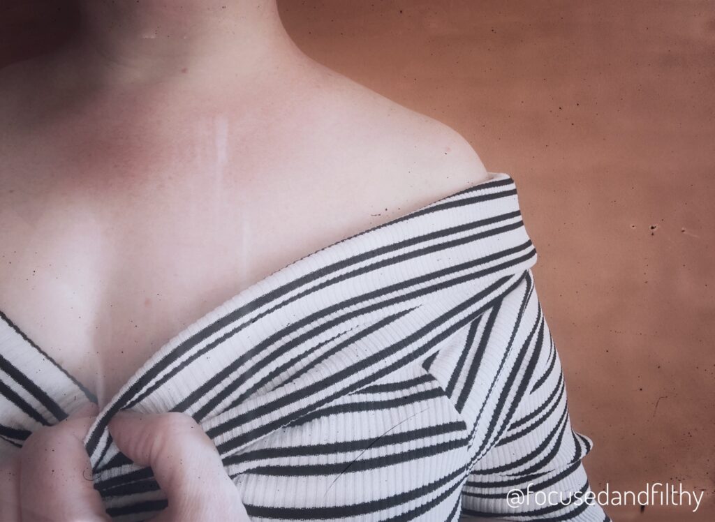 A colour photo of just my left shoulder, I’m wearing an off the shoulder black and white horizontal stripped top and I’m pulling the middle down with some fingers hinting at a cleavage. 