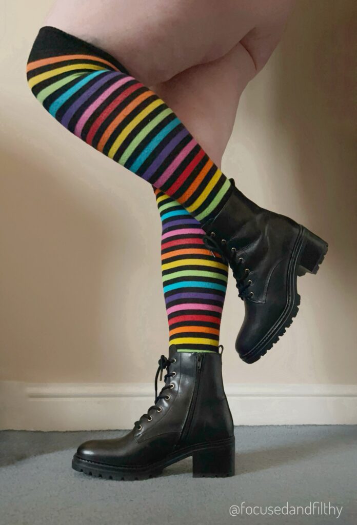 Photo of my legs, I’m wearing over the knee rainbow striped socks and lace up black leather ankle boots that are very new with about an inch thick heavy duty heel 