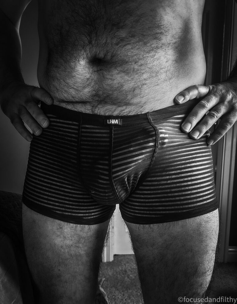 A dark but high contrast black and white photograph of my fellas new Christmas pants. They are snug hockey shorts shaped with in a striped sheer mess pattern and a very large bugling cock underneath 