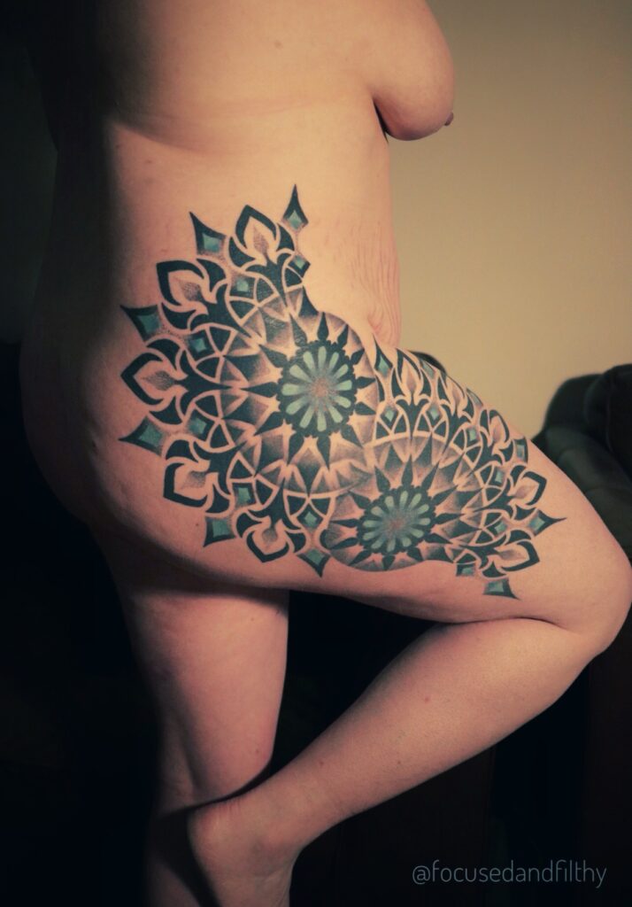 Photograph of my naked side showing a large black and turquoise Mandala tattoo on my right hip and arse making an S shape. 