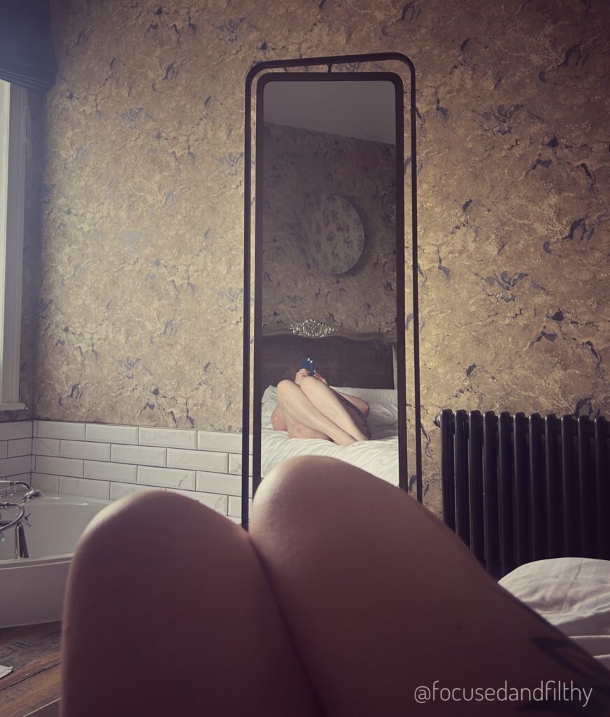 A photograph from my point of view looking down the bed at a tall long mirror angled at the bed reflecting my legs back at me. 